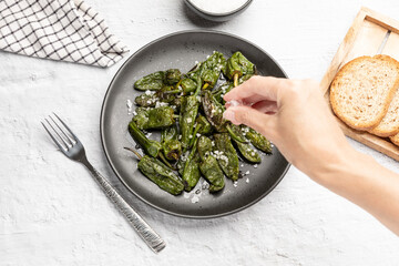 Hand adding salt to spanish food grilled green padron pepper on dish