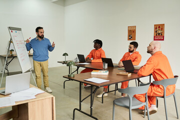 Caucasian middle aged man teaching group of three adult men wearing orange uniforms sitting at...