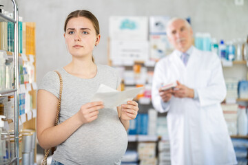 Obraz premium Young pregnant woman holding prescription while pharmacist offering in drugstore
