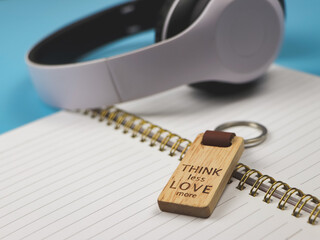  wooden keyring with word "Think less love more" on diary with headphone on blue background.
