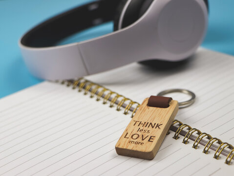 Naklejki  wooden keyring with word "Think less love more" on diary with headphone on blue background.