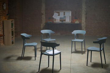 Empty chairs arranged in circle standing in prison room with exposed brick walls and bulletin board...
