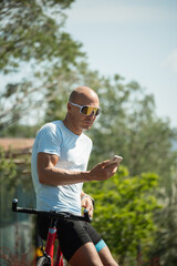 Cyclist relax and standing with smartphone in sunny public park. Outdoor activity. Vertical.