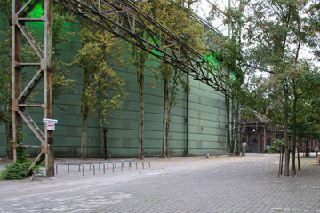 A large industrial building with green-paneled walls and exposed metal structures in...