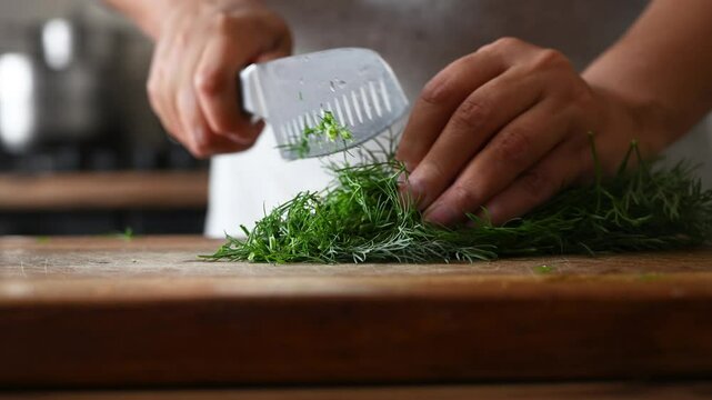Female hands cutting fresh dill on wooden cutting board in kitchen, close-up. Concept of organic food, healthy eating, homemade cooking, food preparation for winter.