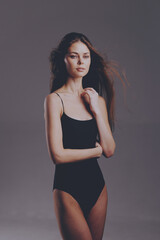 young woman in black bodysuit standing against gray background with a thoughtful expression and...
