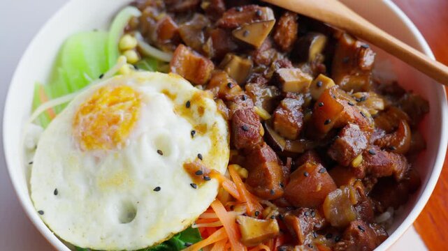 A bowl of braised pork rice topped with a golden fried egg, carrots, and greens&mdash;capturing savory depth, comforting texture, and vibrant plating in Chinese homestyle cuisine.