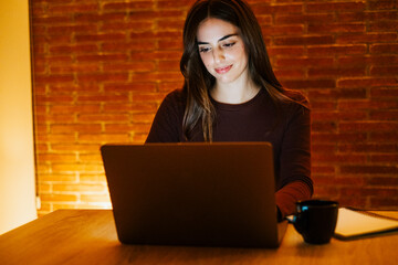 Young woman working late at home with warm lamp light – student or freelancer using laptop for...