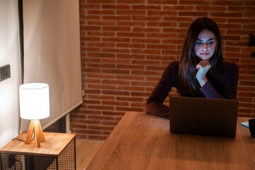 Young woman working late at home with warm lamp light – student or freelancer using laptop for...