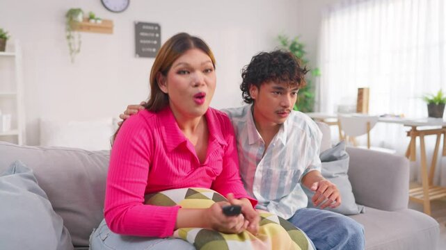Asian excited transgender woman and partner watching news in house. 