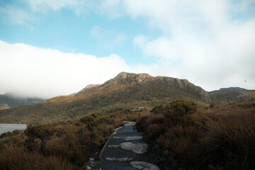 A boardwalk winding beside the serene Dove Lake, with the majestic Cradle Mountain looming in the...