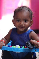 Adorable baby sitting in a blue walker and smiling at the camera