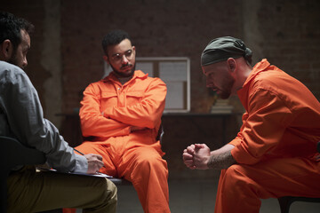 Two young adult men in orange prison uniforms sitting with middle aged Caucasian man leading group...