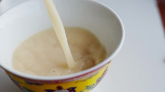 Tibetan butter tea flows into a yellow ceramic bowl with red accents&mdash;highlighting cultural warmth, liquid texture, and traditional beverage ritual.