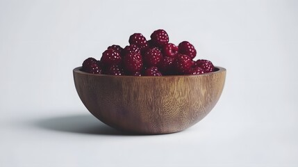 Photograph of a dark wooden bowl filled with ripe raspberries.