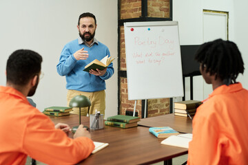 Middle aged Caucasian man teaching poetry lesson to two prisoners wearing orange uniforms in...
