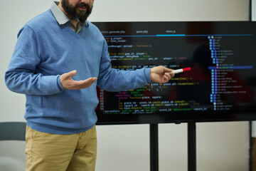 Middle aged Caucasian man teaching programming in prison classroom, holding marker and gesturing in...