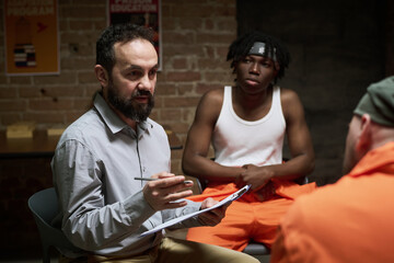 Middle aged Caucasian man holding clipboard and pen conducting group discussion, with Black teenage...