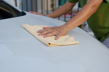 A smiling man is washing his car with soapy water under bright sunlight, showing his enthusiasm and joy in his daily work.