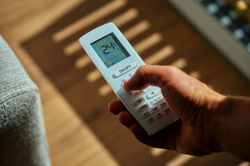 Close-up of person hand holding air conditioner remote control on sunny day with shadows. Adjusting...