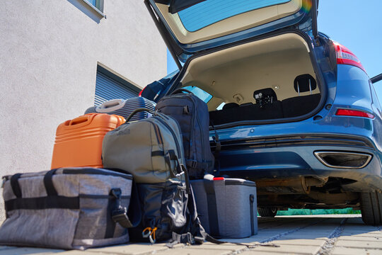 Suitcases and bags in front of open car trunk, standing on pavement near suburban house. Luggage ready for loading in vehicle before travel or moving. Concept of relocation or road trip