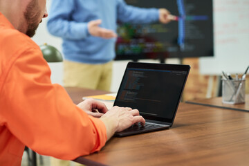 Caucasian man in orange prison uniform using laptop during classroom lesson, instructor standing near digital screen explaining educational material in prison setting