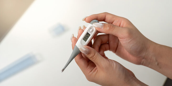 Health Monitoring. Woman checking temperature with digital thermometer at home.