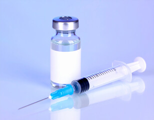 Vial with a blank label and a syringe with a needle, on a light blue surface.