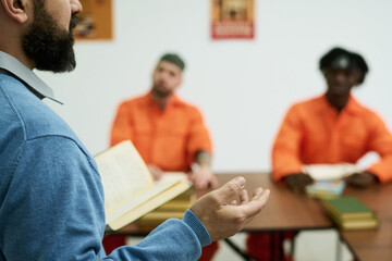 Middle aged Caucasian man holding open book leading discussion, with two young adult men in orange...