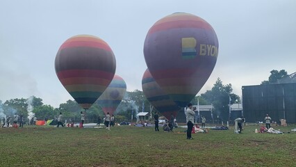 Colorful hot air balloons festival display distinct horizontal stripes are being inflated on the cloudy sky provide  backdrop. 