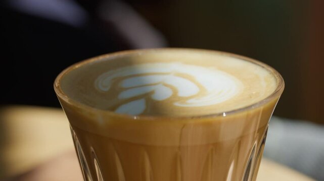 A latte with elegant leaf foam art sits on a wooden tray bathed in window light&mdash;evoking warmth, minimalist charm, and the intimate rhythm of a tranquil morning caf&eacute; moment.