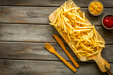 Fast food restaurant concept. French fries on cutting board near sauces on wooden table top-down...