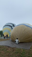 Colorful hot air balloons festival display distinct horizontal stripes are being inflated on the cloudy sky provide  backdrop. 