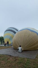 Colorful hot air balloons festival display distinct horizontal stripes are being inflated on the cloudy sky provide  backdrop. 