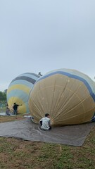 Colorful hot air balloons festival display distinct horizontal stripes are being inflated on the cloudy sky provide  backdrop. 