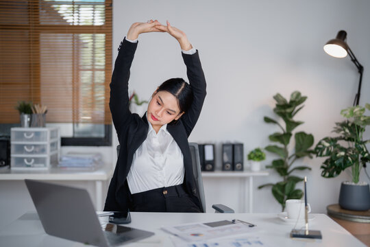 Asian businesswoman relaxing and stretching her arms at her workplace, taking a well-deserved break after long hours working on a laptop, promoting health and wellness in the office - Powered by Adobe