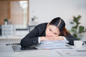 Exhausted businesswoman resting her head on a large stack of documents, overwhelmed by paperwork...