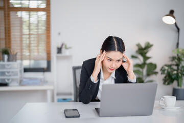 Young businesswoman having a bad headache and massaging her temples while working on a laptop in a...