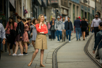 A woman stands thoughtfully in the middle of a crowded street. Lost in her own thoughts, she seems...