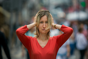 A close-up portrait of a woman standing in the middle of a crowded street, covering her ears with...