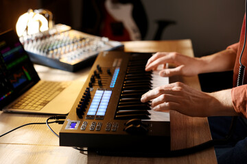 Man working with MIDI keyboard at wooden table indoors, closeup