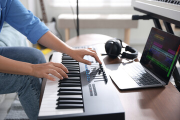 Woman working with MIDI keyboard at table indoors, closeup
