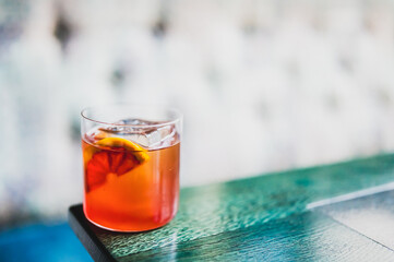 Refreshing cocktail with ice cubes and blood orange slice in a clear glass on a wooden table, with soft natural lighting and a blurred background.