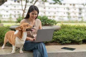 Remote Work and Pet Companionship. Woman smiling while using laptop with her corgi dog nearby.