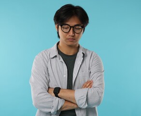 Handsome Asian man in glasses with crossed arms on light blue background