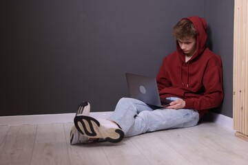 Cyber bullying. Upset teenage boy with laptop on floor indoors. Space for text