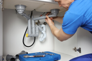 Plumber fixing pipes under sink indoors, closeup