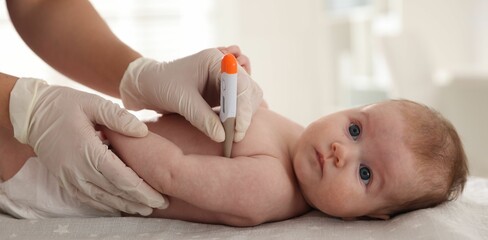 Pediatrician examining baby with thermometer at table in clinic, closeup