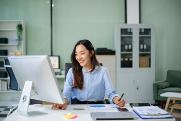 Asian businesswoman analyzes data charts on her desktop in a modern office, showcasing professional productivity, digital innovation, and real people
