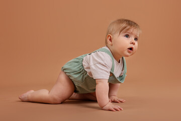 Cute little baby crawling on pale brown background